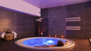 A spa room with a hot tub, wooden flooring, a decorative wall, and a towel on a basket. - Hôtel Le Neptune (Propriano)