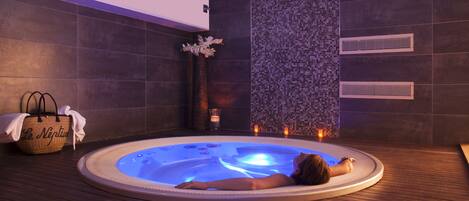 Een spa-ruimte met een jacuzzi, houten vloeren, een decoratieve wand en een handdoek in een mand.
