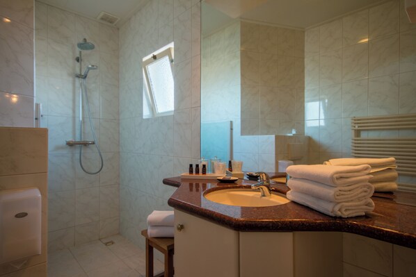 Ein Badezimmer mit einer dusche aus Marmorplatten, einem Waschbecken mit Spiegel und gestapelten Handtüchern auf der Ablagefläche.