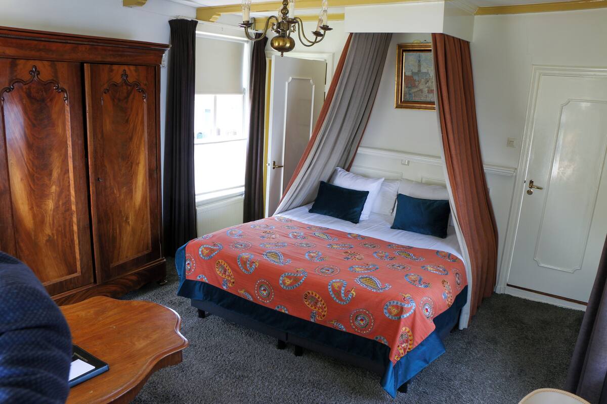A bedroom with a four-poster bed, a wooden wardrobe, and a desk with a chair.