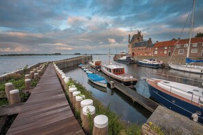 Une jetée en bois où sont amarrés des bateaux, un bâtiment en pierre avec des toits rouges et un ciel nuageux.