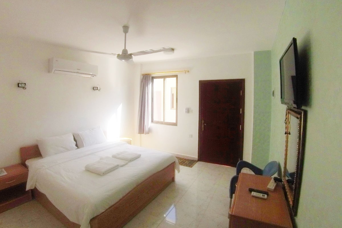 A hotel room with a bed, a desk, a television, and a door.