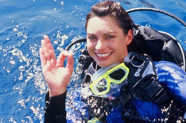A person in a blue wetsuit with yellow goggles and a black backpack, partially submerged in water.