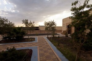 A courtyard with a tiled walkway, palm trees, and a building with a beige facade.