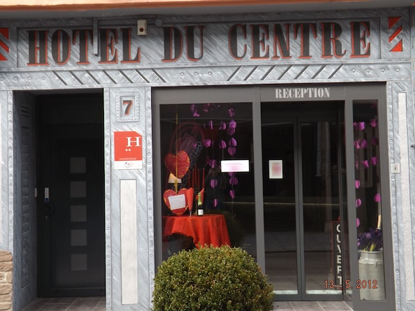 L’entrée d’un hôtel, avec un comptoir de réception, une enseigne indiquant le numéro de chambre 7 et un tampon indiquant la date du 13 mai 2012.