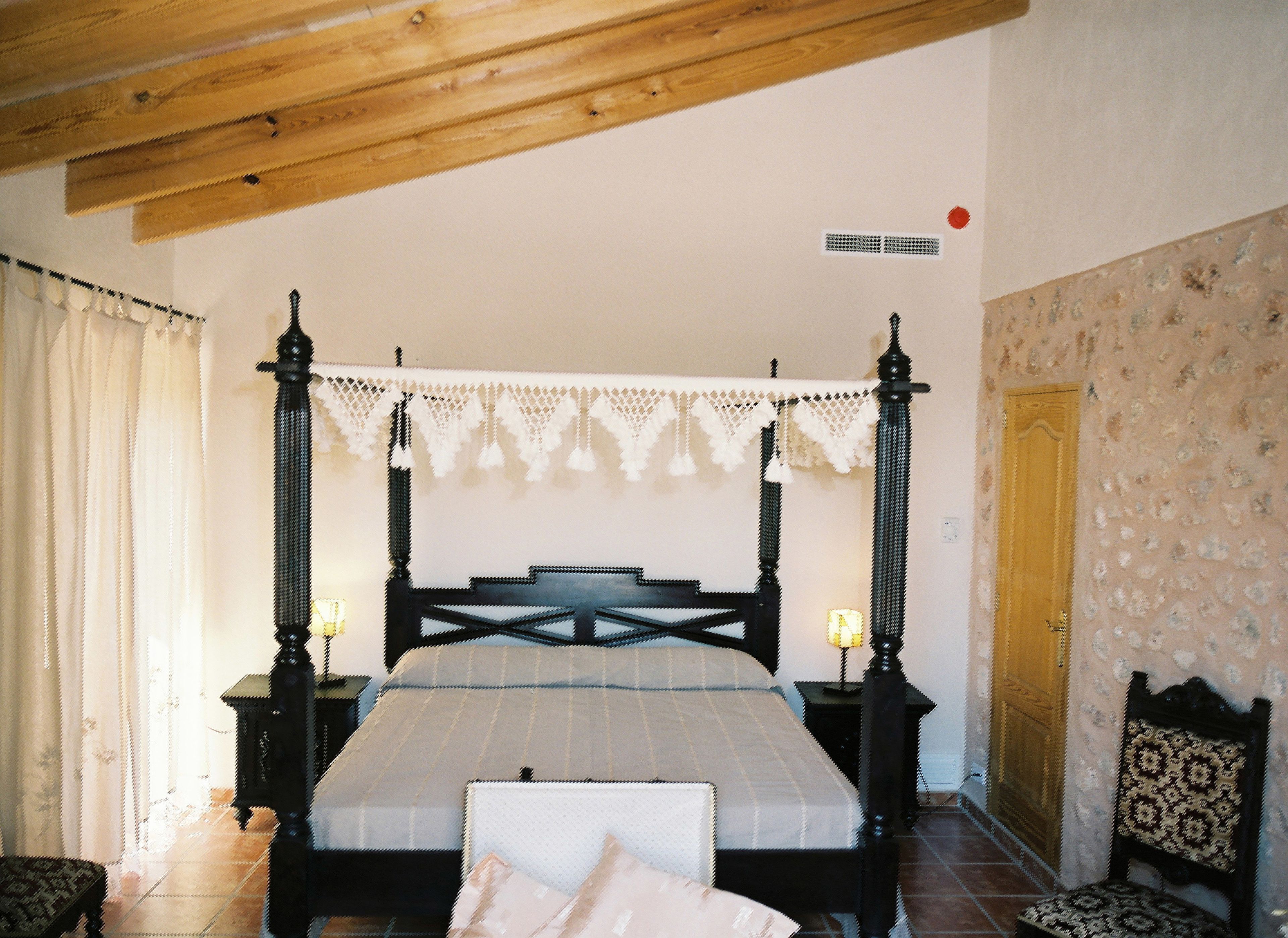 Ein Himmelbett mit Spitzenvorhang, Holzboden, Wand mit Muster und Holztür.