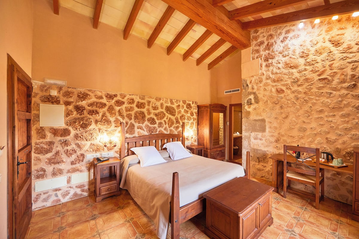 Ein Schlafzimmer mit Steinwand, Holzbettgestell, Nachttischen und einer Holzbank.