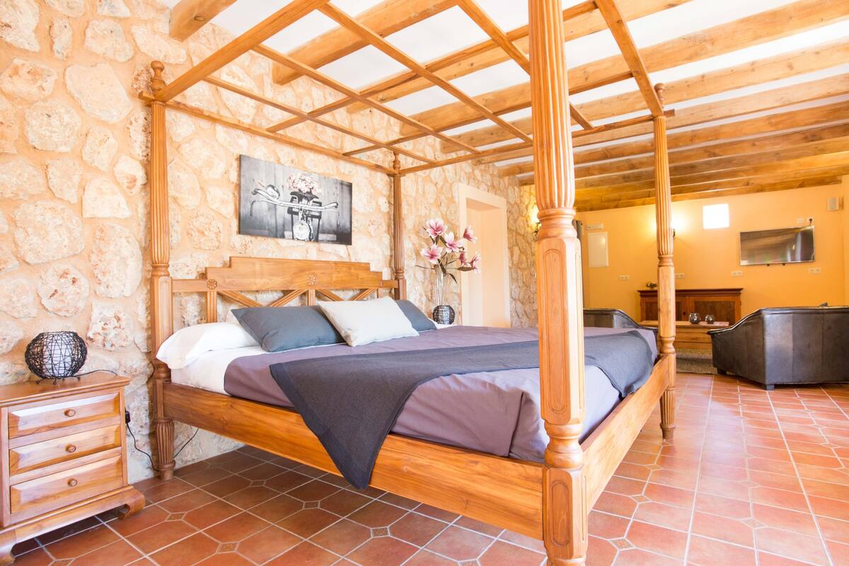 Ein Himmelbett mit einer Wand aus Stein, einem Nachttisch aus Holz und einem gefliesten Boden.