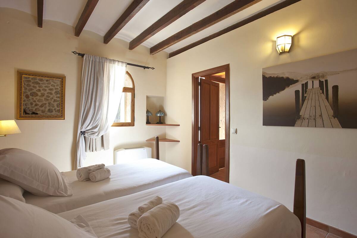 Ein Hotelzimmer mit zwei Betten, einer Holzbalkendecke, einem Gemälde eines Piers und einer Wandleuchte.