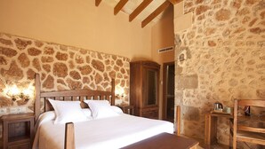 A bedroom with a stone wall, wooden bed frame, bedside tables, and a wooden bench. - Agroturismo Es Quatre Cantons (Binissalem)