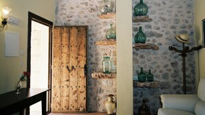 A room with a wooden door, a stone wall with shelves holding green glass bottles, a white chair, and a table with a glass. - Agroturismo Es Quatre Cantons (Binissalem)