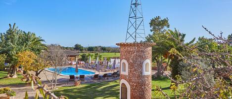 A pool area with lounge chairs and a stone tower with a windmill.