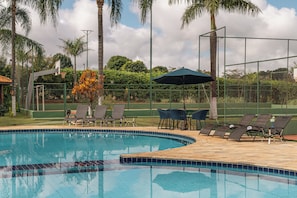 Piscina com borda azulejada, cercada por espreguiçadeiras e uma mesa com guarda-sol.