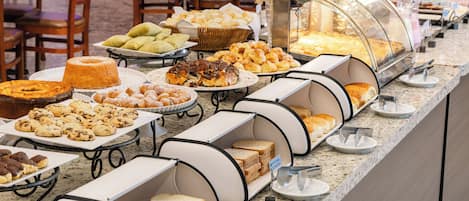 Un bufé con diversas opciones de comida, incluyendo bollería, pan y postres.