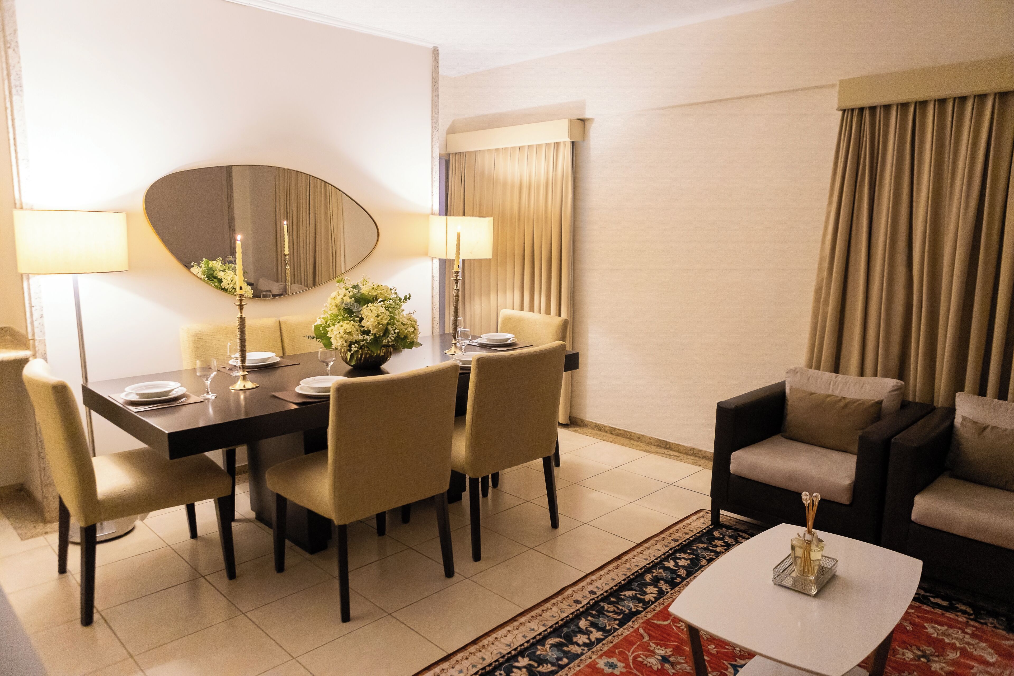 A hotel room with a dining table set for four, a sofa, a coffee table, and a large mirror.