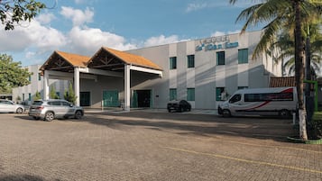 Un hotel con acceso cubierto, varios coches aparcados y una furgoneta en la entrada.