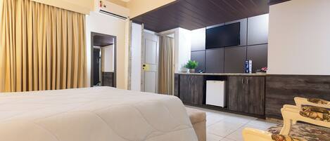 A hotel room with a large bed, a small kitchenette, and a dining area with chairs.