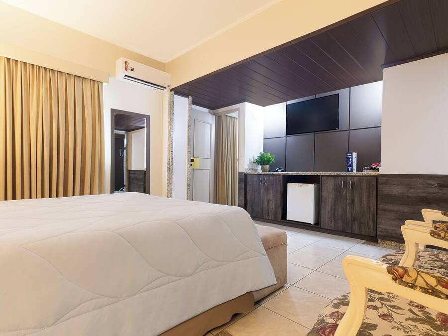 Una habitación de hotel con una cama grande, una kitchenette pequeña y una zona de comedor con sillas.