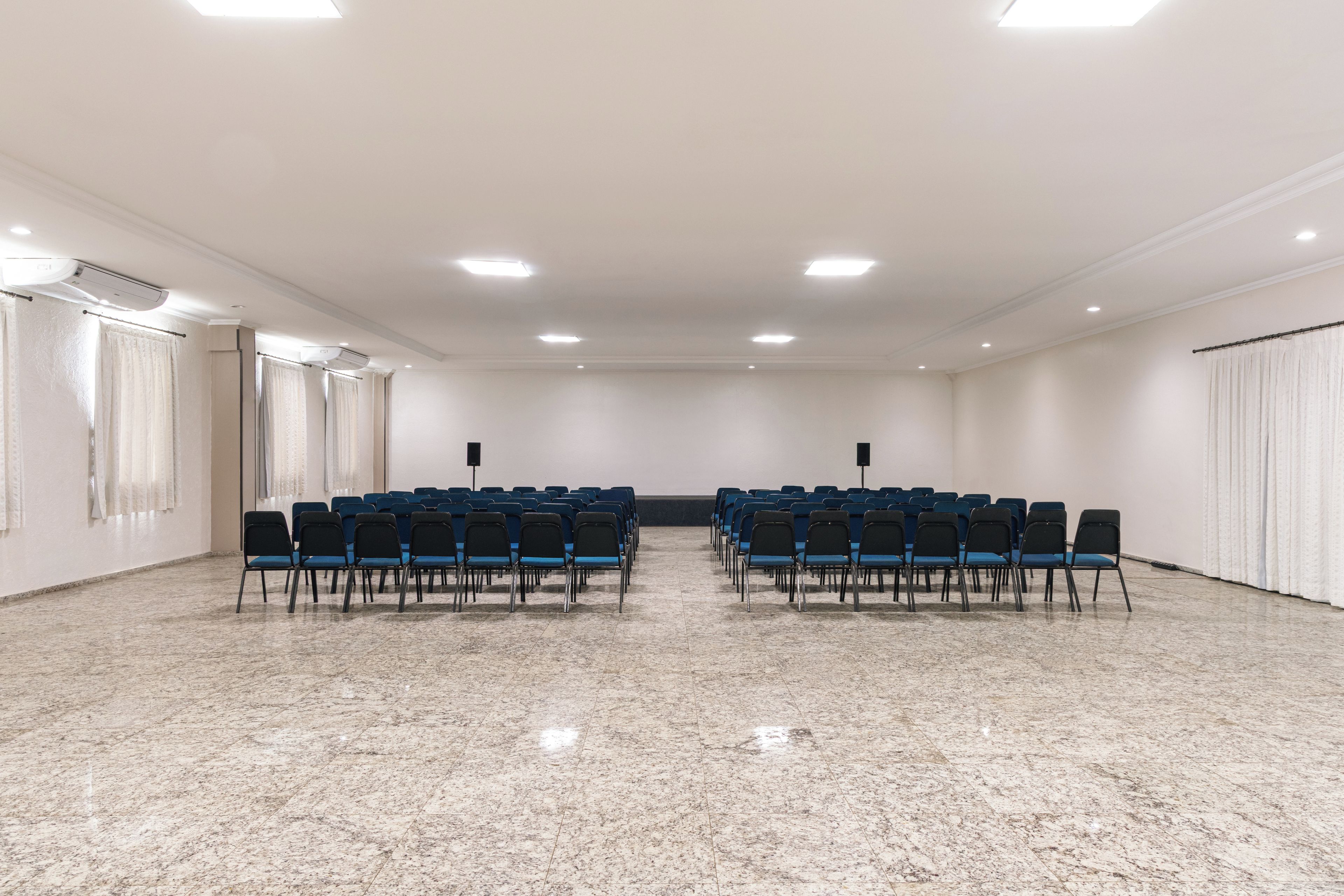 A conference room with rows of chairs, a marble floor, and ceiling lights.