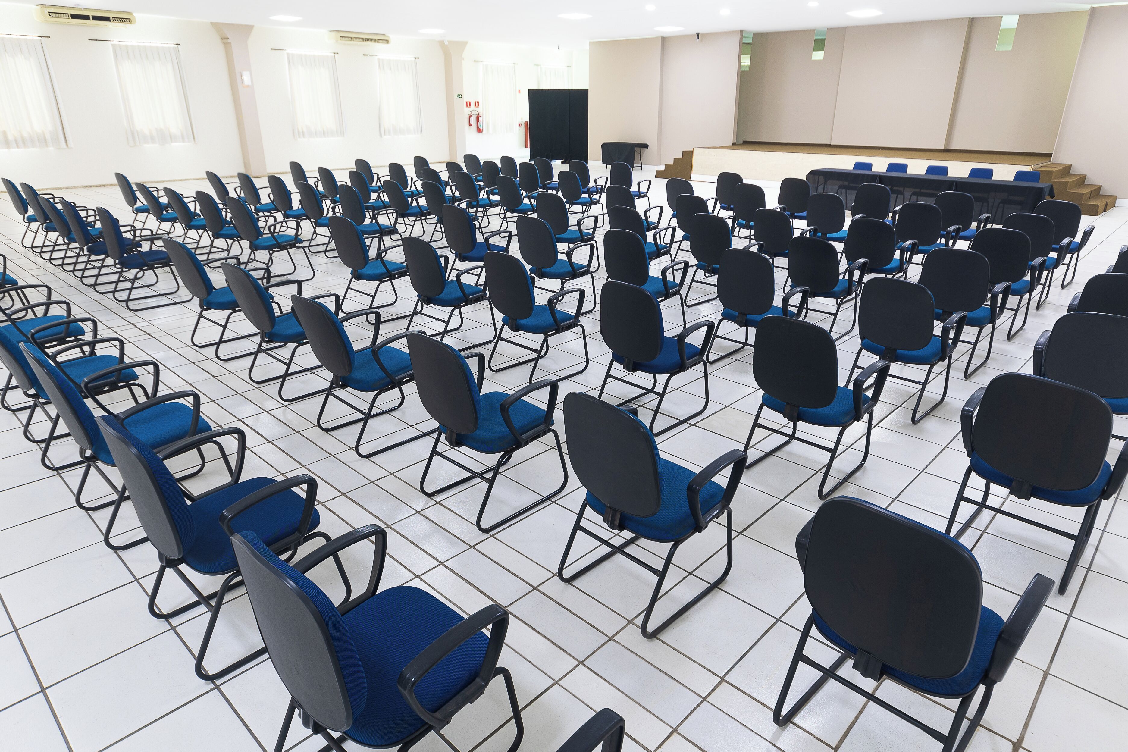 Un salón de conferencias con filas de sillas azules y una zona de escenario.