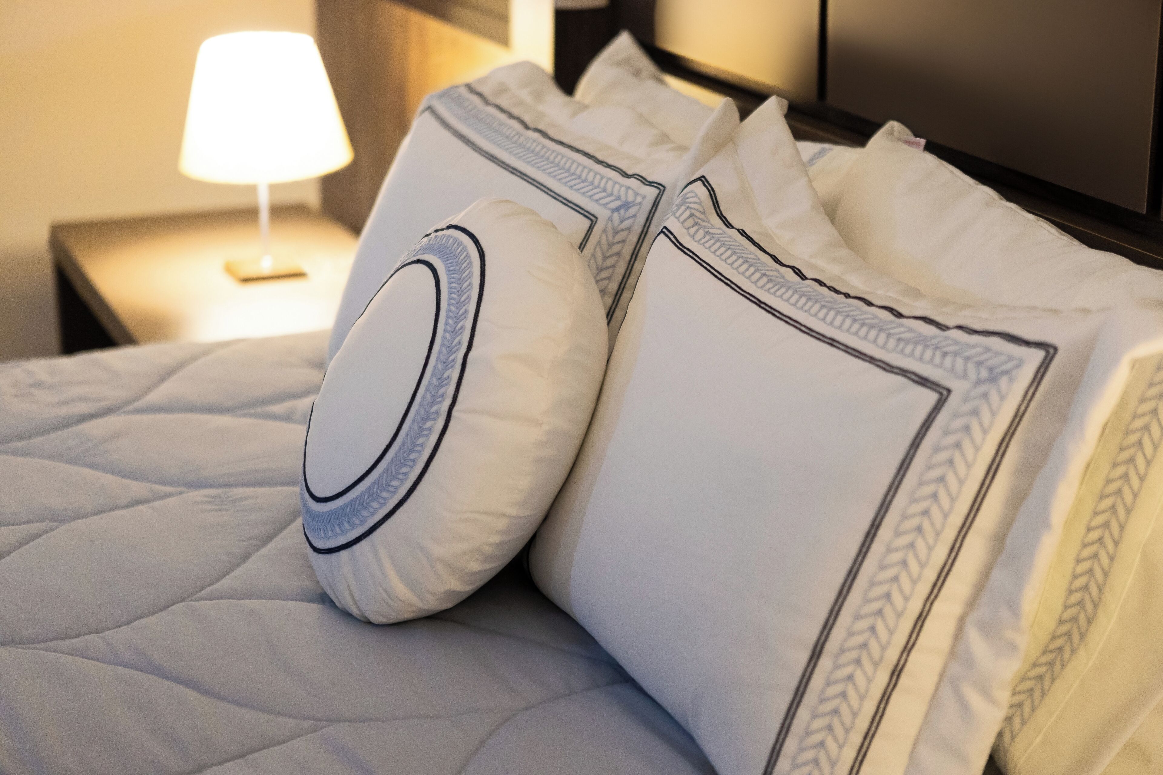 Un lit bien fait, avec du linge de lit blanc et des coussins décoratifs.