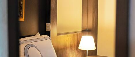 A neatly made bed with a white quilt and a single pillow, a bedside table with a lamp, and a framed picture on the wall.