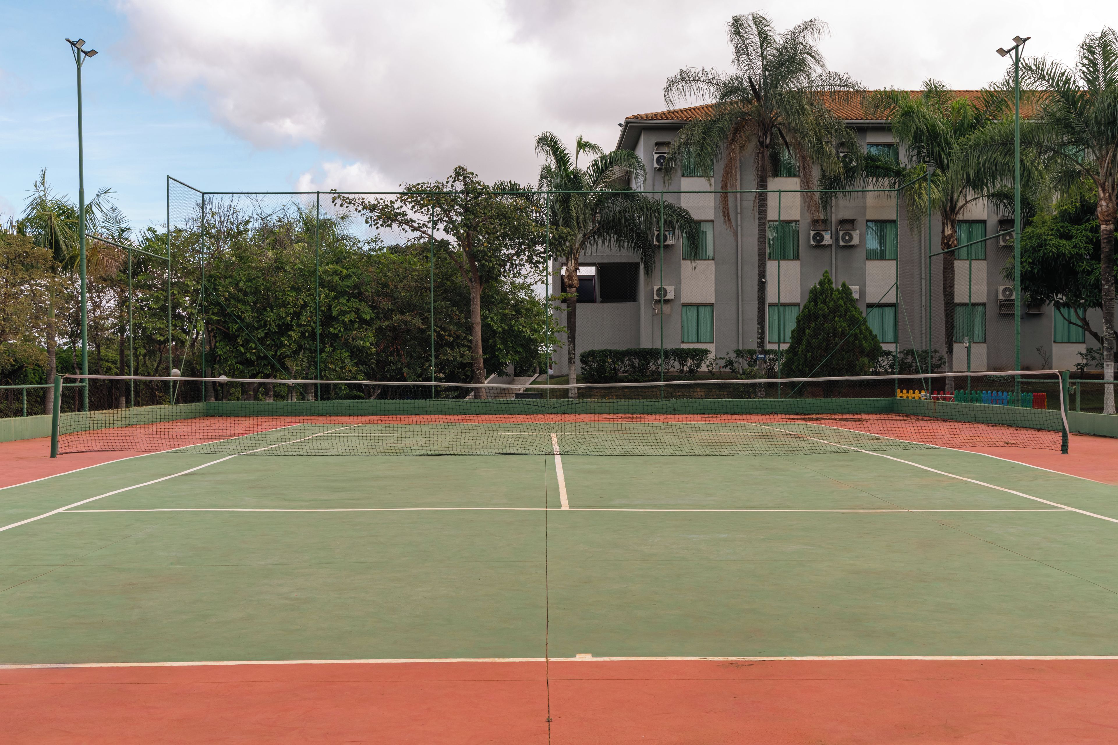 A tennis court with a net, surrounded by a fence and trees.