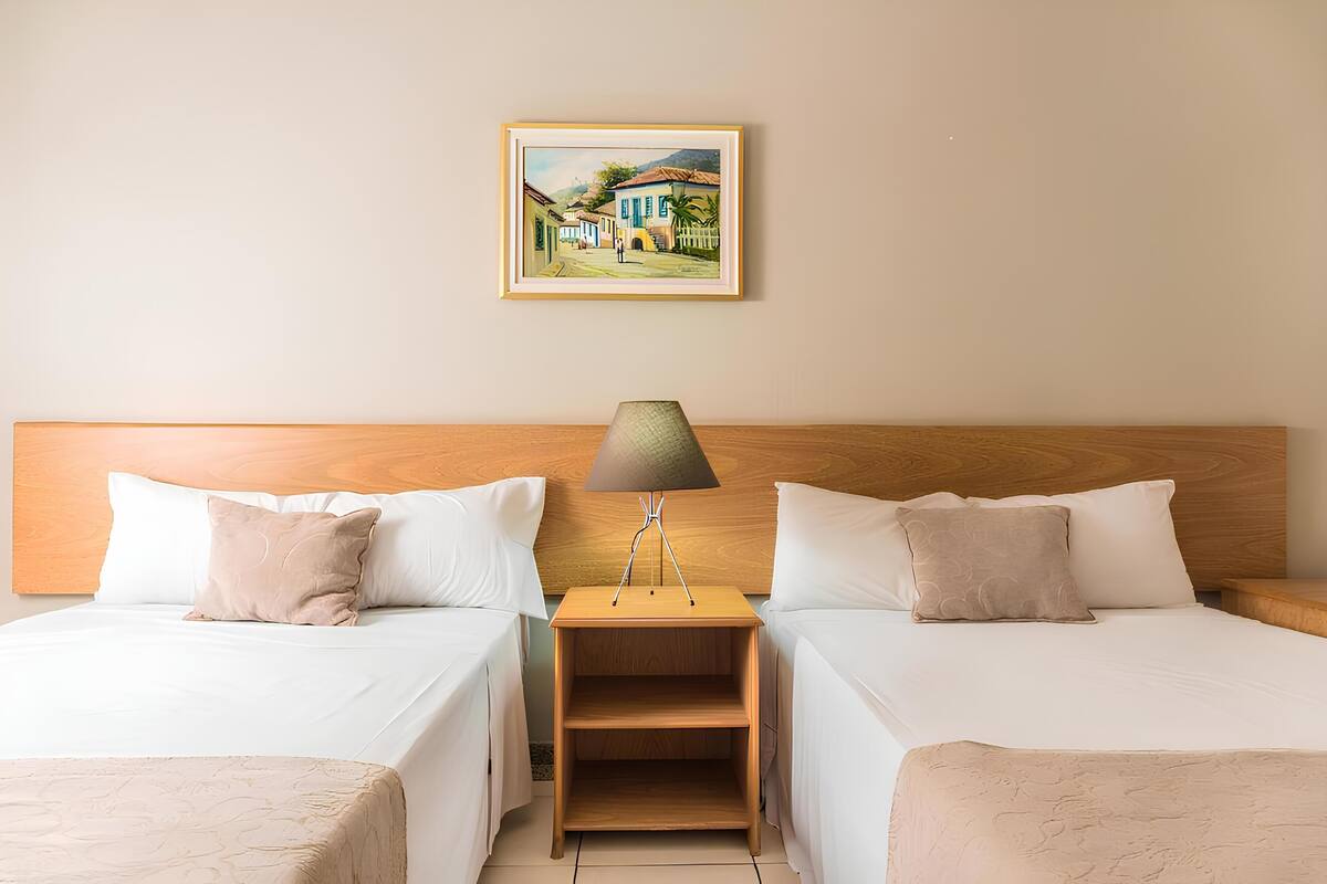 A hotel room with two single beds, a wooden headboard, a nightstand with a lamp, and a framed picture on the wall.