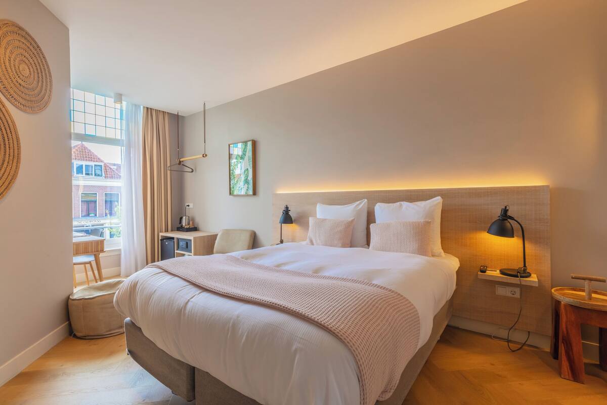 Une chambre d’hôtel moderne avec un grand lit, des lampes de chevet, une petite table et une vue sur l’extérieur.