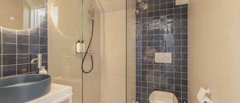 A modern bathroom with a glass-enclosed shower, a round sink, and a toilet.