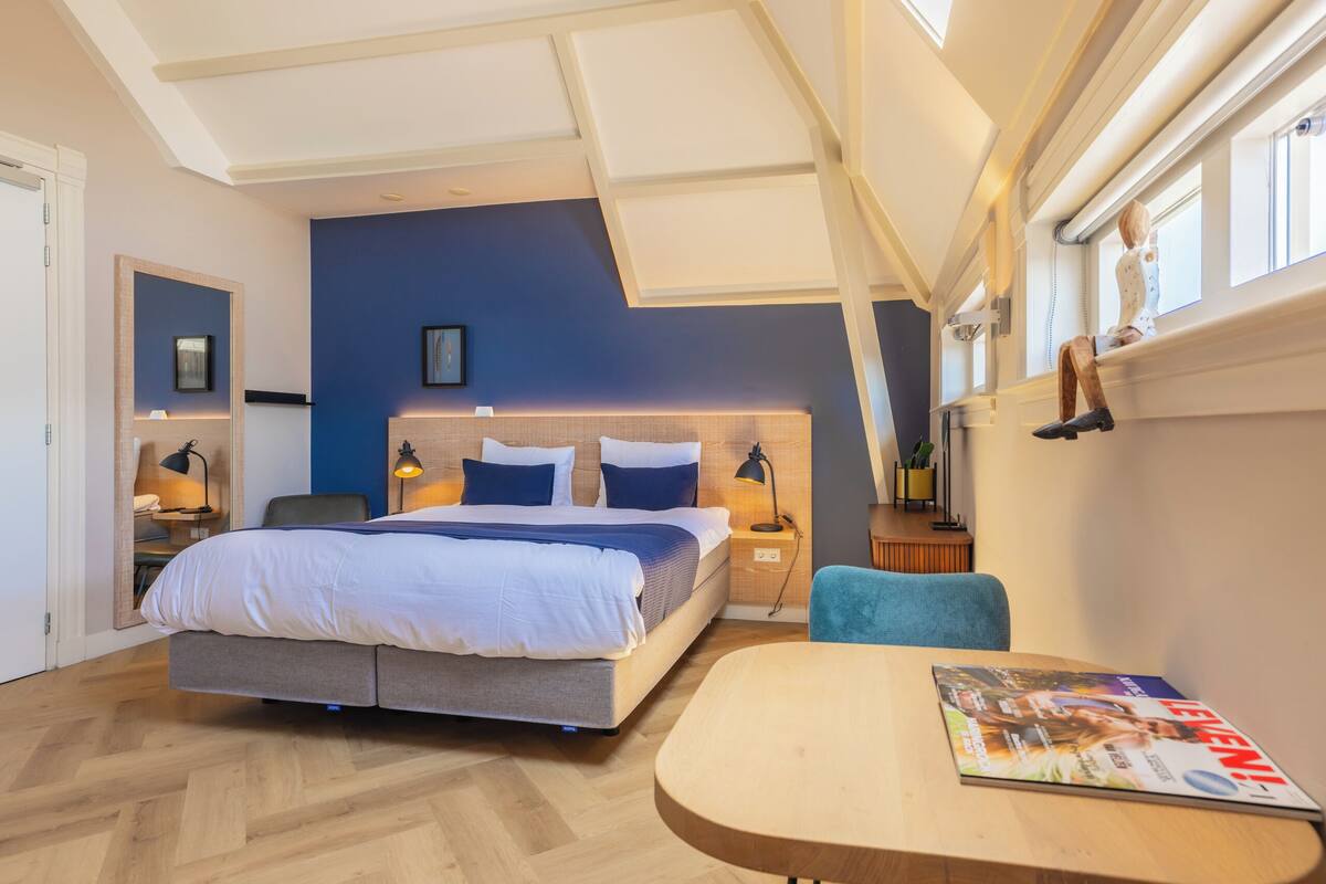 Une chambre moderne avec un grand lit, des tables de chevet, un bureau et une fenêtre donnant sur un beau paysage.