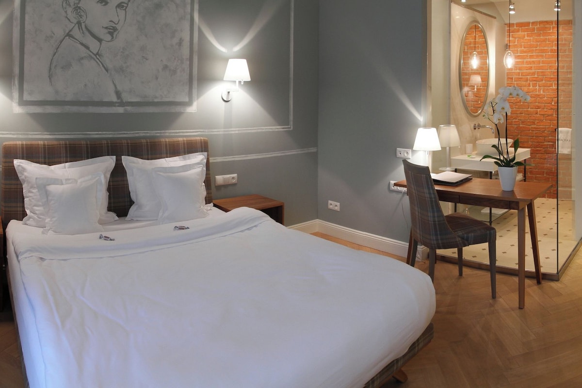 Habitación de hotel con cama, escritorio y silla, baño con espejo y puerta.