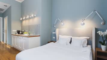A hotel room with a bed, bedside tables, a nightstand, a desk with a kettle, and a mirror.