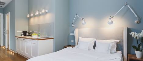 A hotel room with a bed, bedside tables, a nightstand, a desk with a kettle, and a mirror.