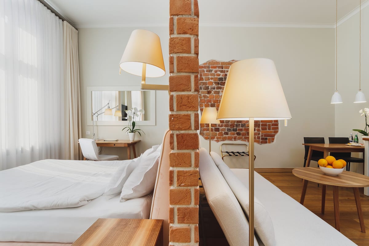 Ein Hotelzimmer mit Ziegelfassade, einem Bett, einem Schreibtisch, einem Stuhl, einem Esstisch mit Stühlen und einer Obstschale.