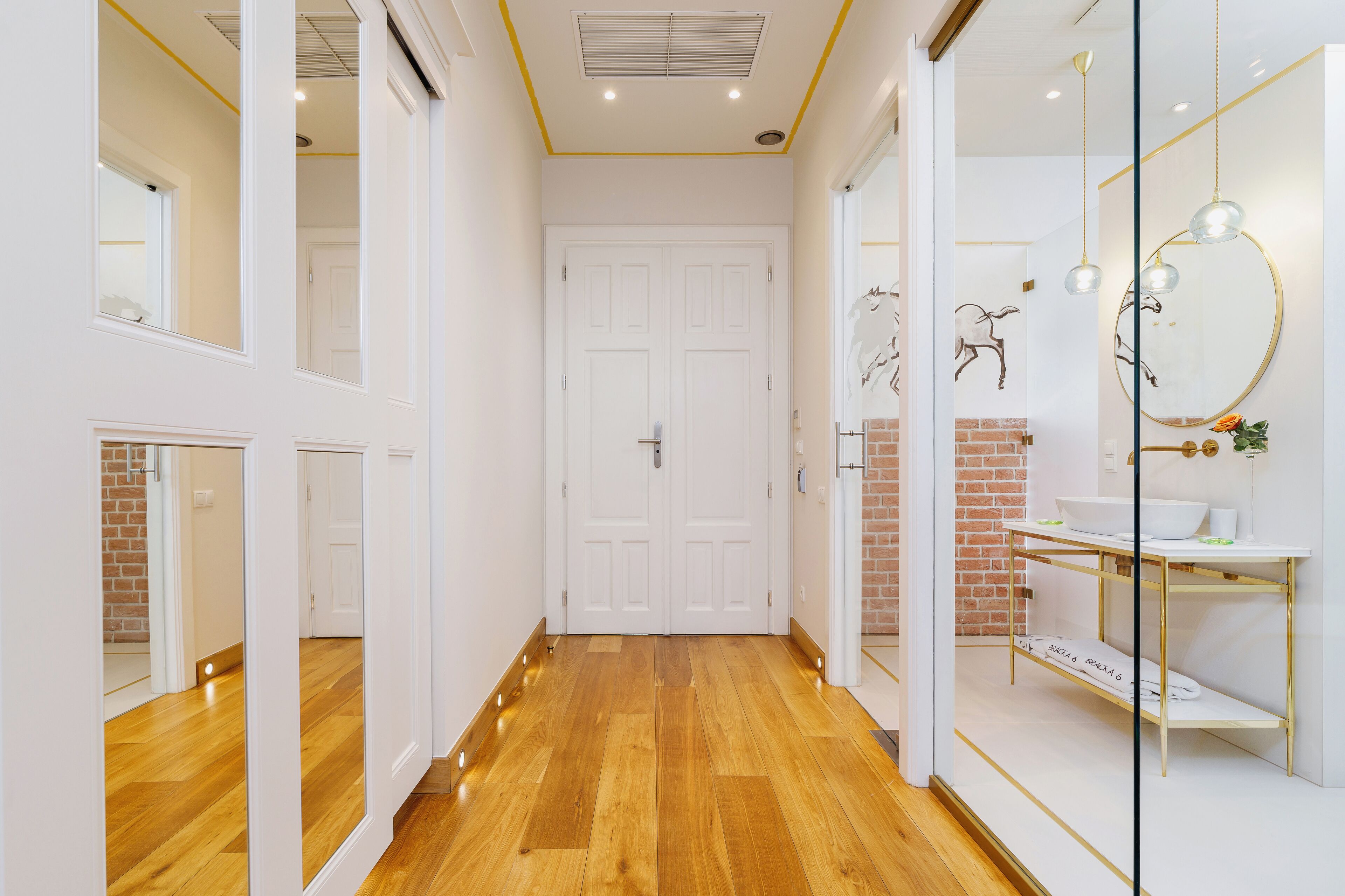 A hallway with wooden flooring, white doors, and a glass partition with a mirror and decorative items.