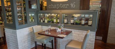 Interior de un restaurante con pared de ladrillo, un letrero que dice 'chapter 16' y una zona de bar con botellas de vino.