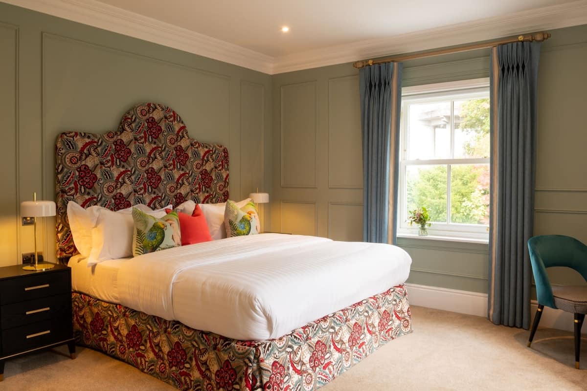 A bedroom with a large bed, a nightstand, a chair, and a window with curtains.