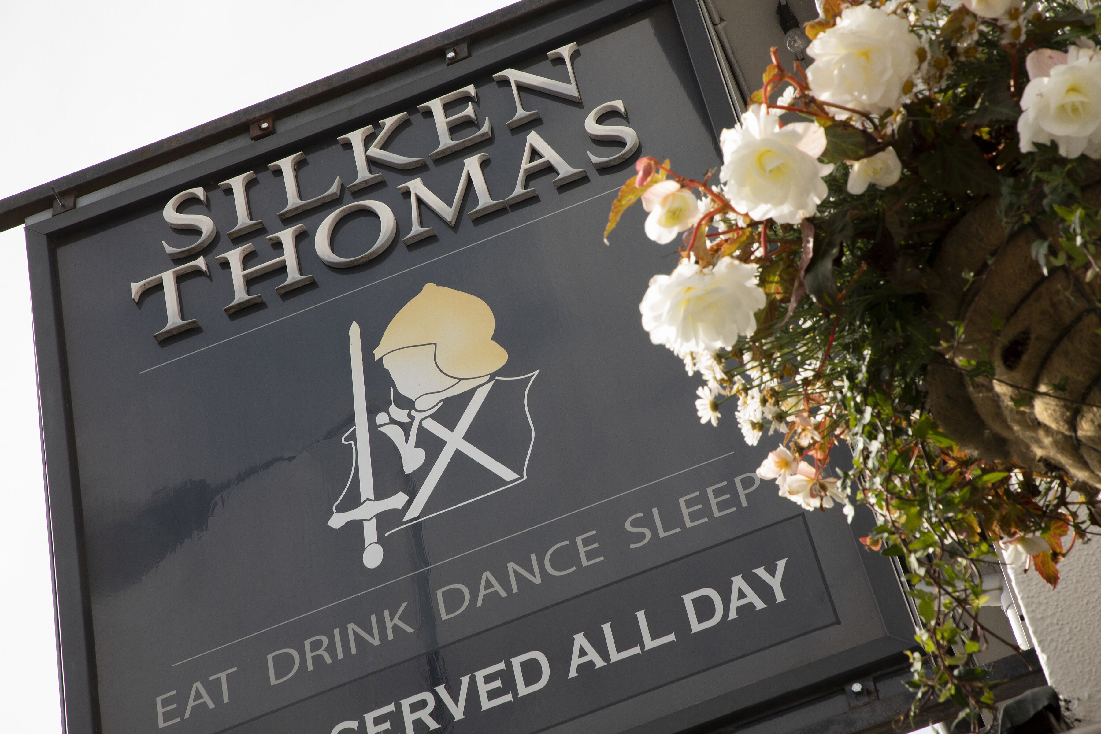 Letrero de 'Silken Thomas' con un icono de baile y el texto 'COMER BEBER BAILAR DORMIR. SERVICIO TODO EL DÍA'.