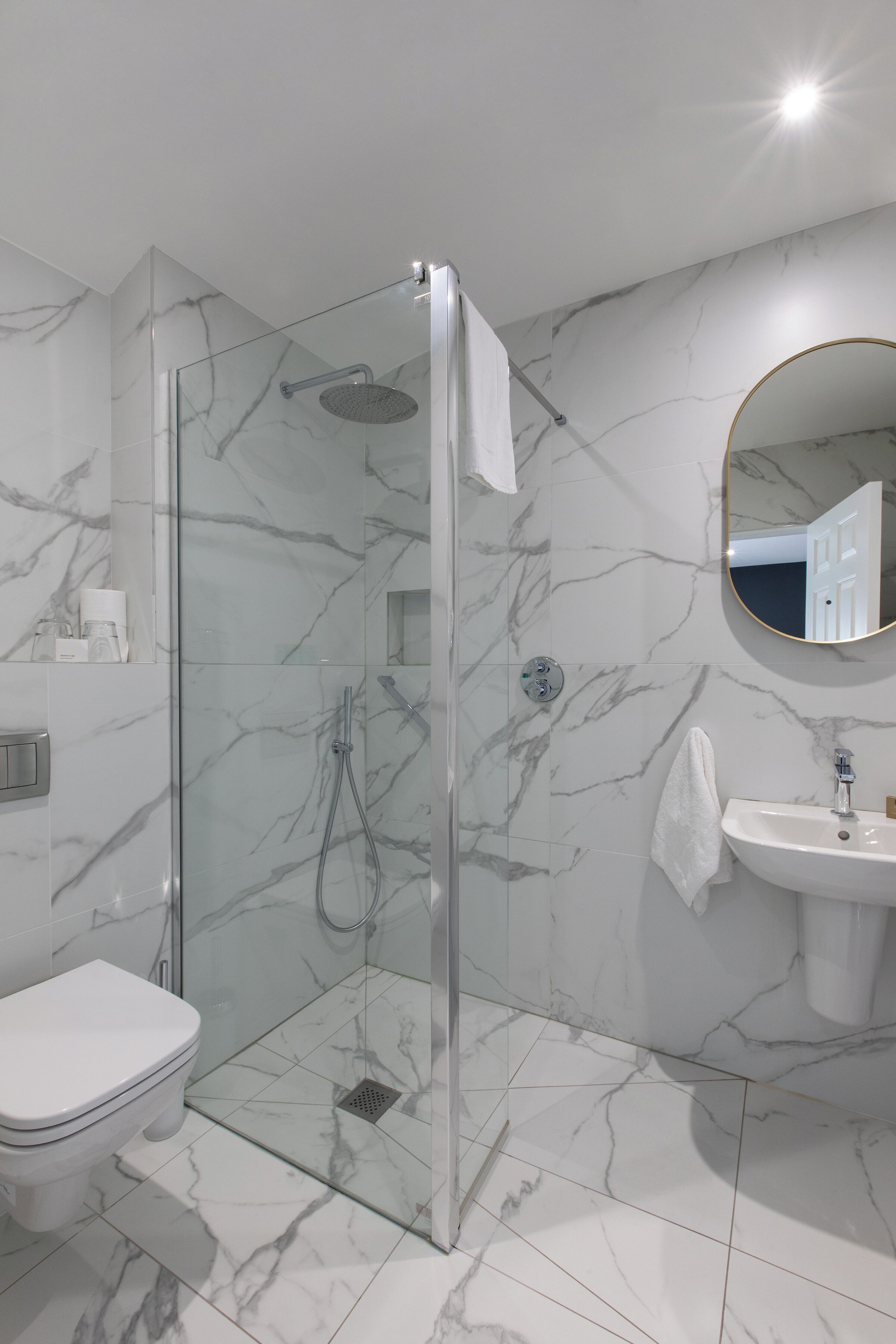 Un baño moderno con ducha envuelta en vidrio, un inodoro blanco y un lavabo con un espejo encima.