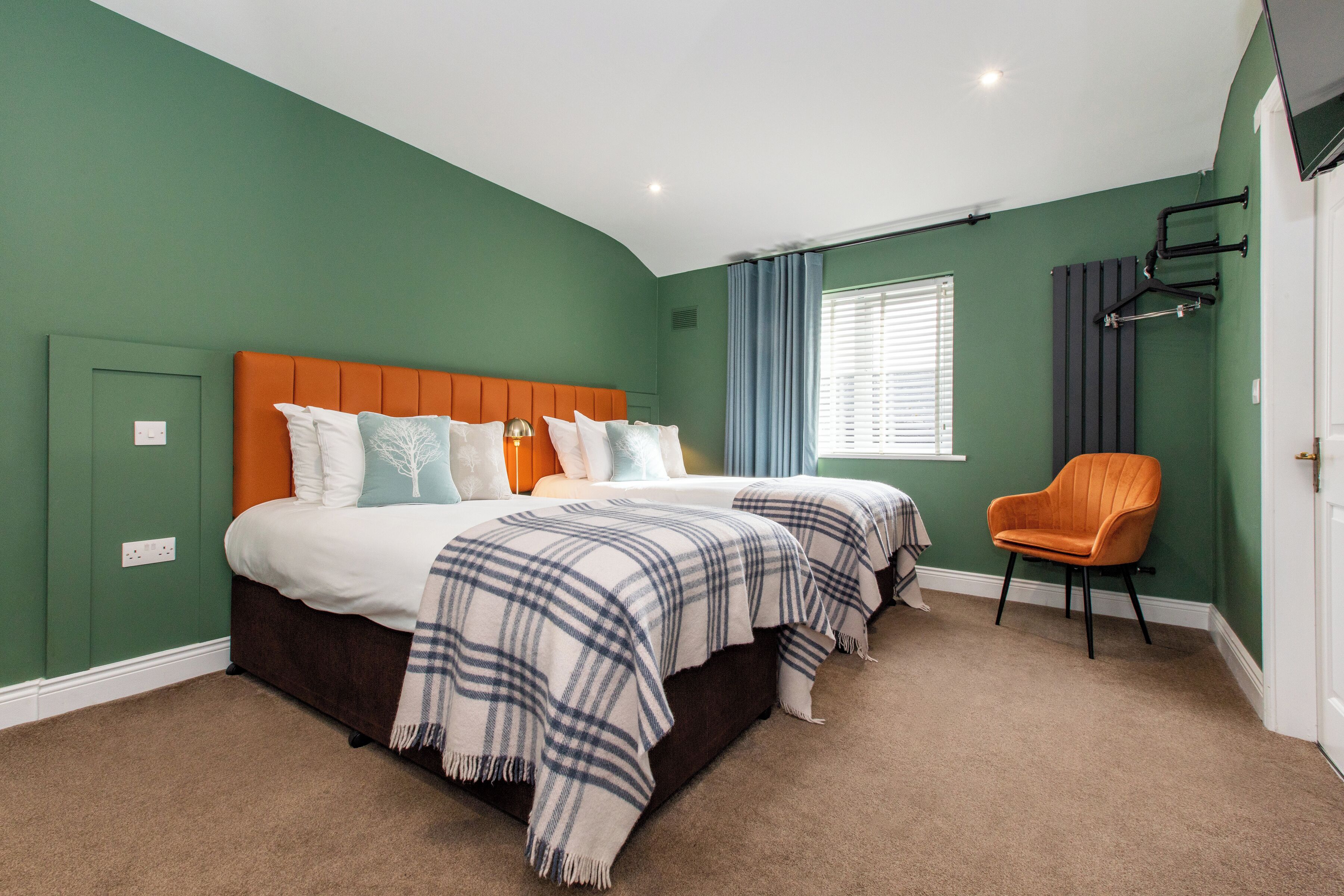A bedroom with two beds, a chair, and a window with curtains.