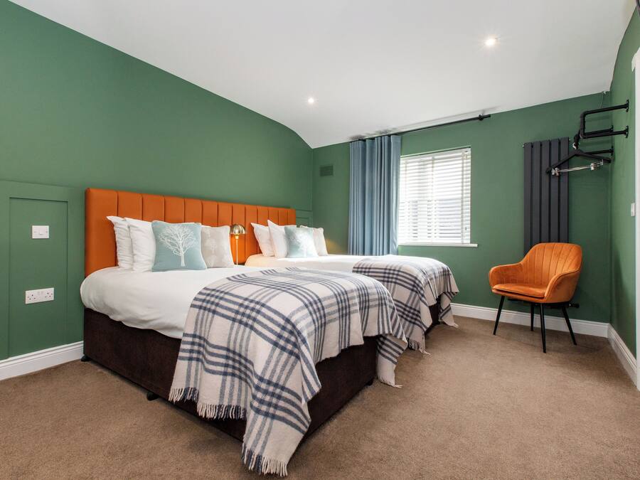 A bedroom with two beds, a chair, and a window with curtains.