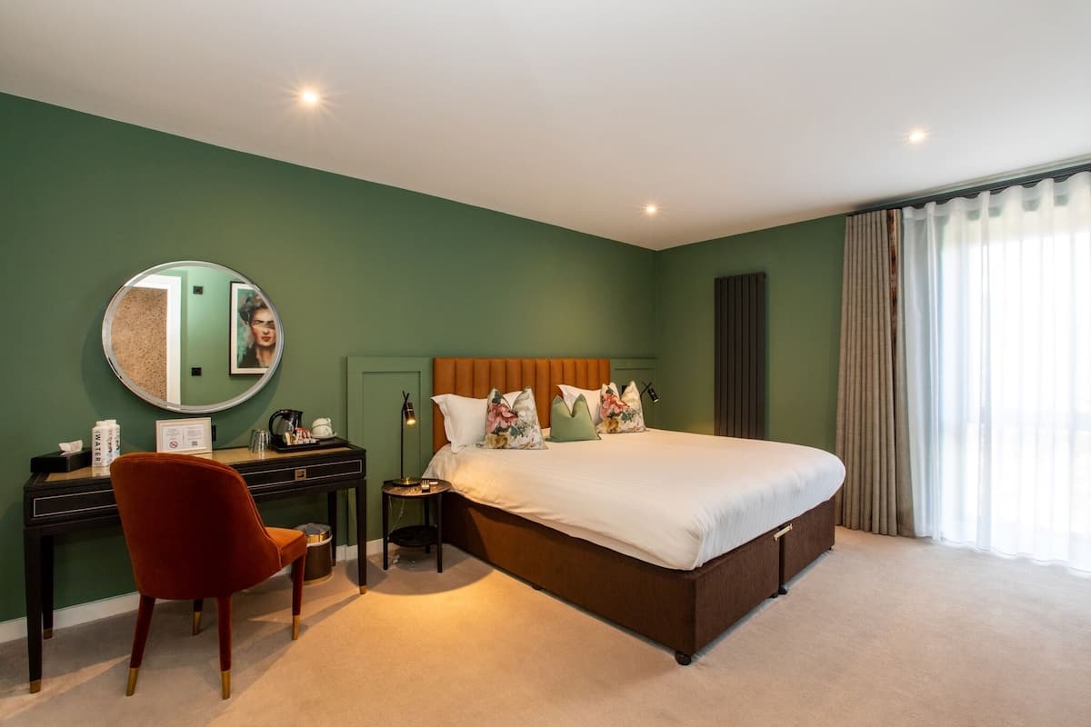 A bedroom with a large bed, a desk with a chair, a round mirror, and a nightstand.