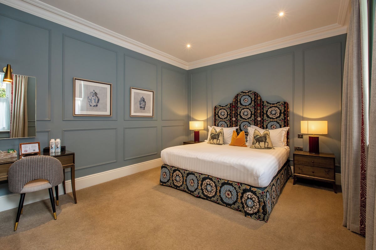 A bedroom with a large bed, two bedside tables, a chair, and framed artwork on the walls.