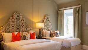 A hotel room with two beds, a nightstand with a lamp, patterned headboards, and a window with curtains. - Silken Thomas (Kildare)