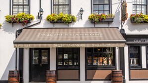 A building with a sign reading "SOUTRES GANNON" and a website address. There are flower boxes on the windows and wooden barrels outside. - Silken Thomas (Kildare)