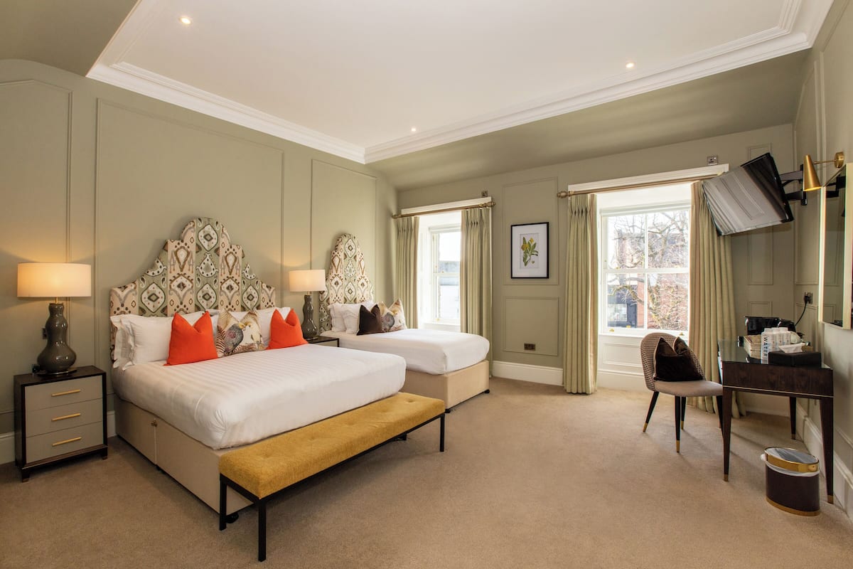 A hotel room with two beds, a desk, a chair, a TV, and a window with curtains.