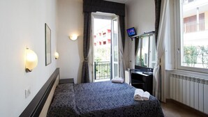 A hotel room with a bed, a desk, a TV, and a window with curtains. - Brenta Milano (Milan)