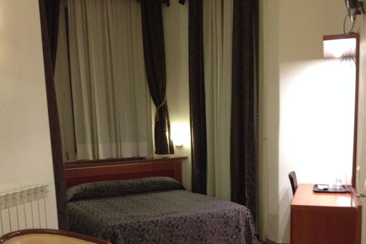 Una habitación de hotel con una cama, una silla, un escritorio y una lámpara.