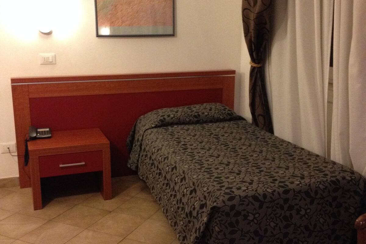 Un dormitorio pequeño y ordenado con una cama individual, una mesita de noche y un cuadro colgado en la pared.